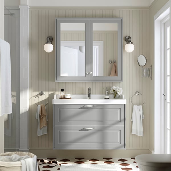 Modern bathroom with RUTSJÖN grey vanity, mirror, shower, and ceramic basin. White accents, wall lights, and chrome towel rings.