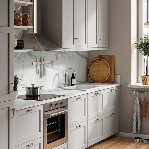 Modern kitchen with white SIBBARP walls and marble backsplash. Neatly organised cabinets, natural accents, and greenery enhance its inviting ambiance.