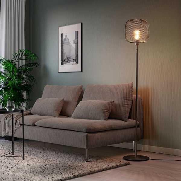 Modern living room with SKAFTET lamp beside sofa, warm light, plant, picture.