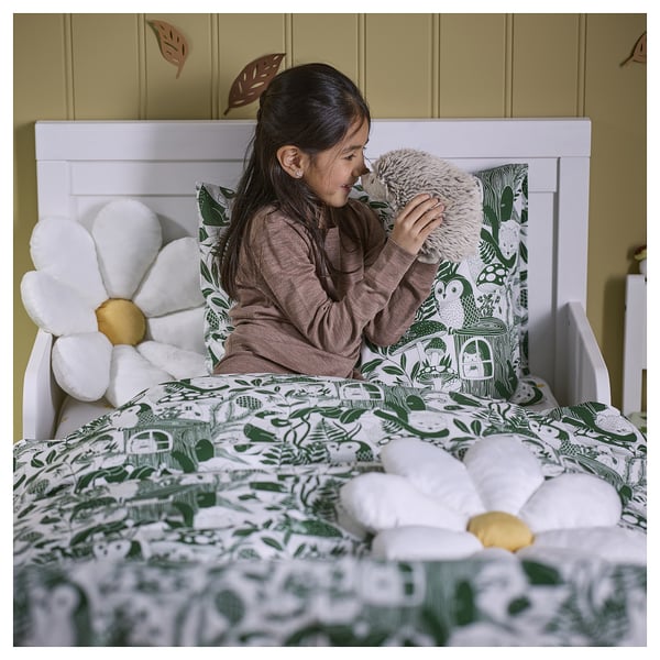 Girl kisses stuffed toy on bed with green leaf sheets and recycled polyester daisy pillows.