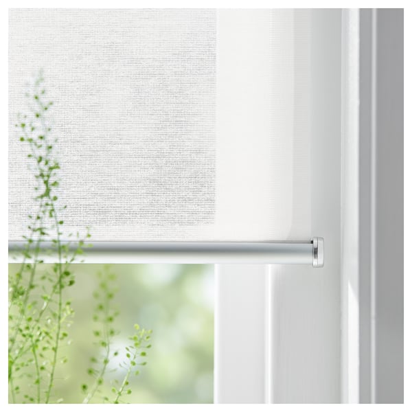 White roller blind, SKOGSKLÖVER brand, partially rolled, in white window frame, showing green plant outside.