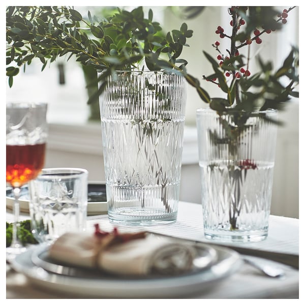 Three elegant, clear glass vases with diamond patterns hold greenery and berries, set on a white table with a plate of food.