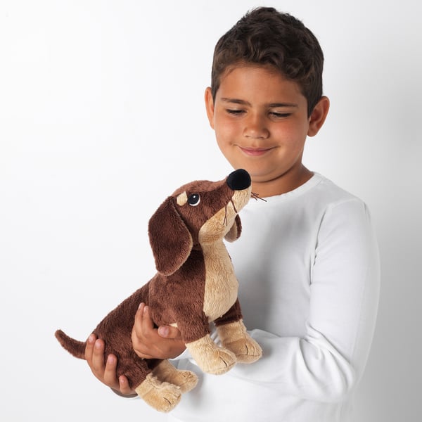 A boy smiles while holding a soft, brown, plush dachshund toy; perfect for cuddling and play.