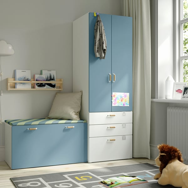Kids room with blue-white SMÅSTAD storage, cushioned bench, wooden shelf, stuffed toy, rug, large window.