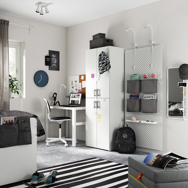 Modern teen bedroom with white SMÅSTAD wardrobe, desk, grey sofa, striped rug, wall clock, and black accessories.