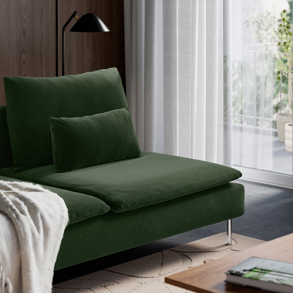 Green upholstered chaise lounge with cushions beside a window, offering a cosy relaxation spot.