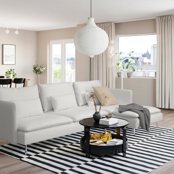 A modern living room with a white SÖDERHAMN sofa and black coffee table on a striped rug, with large windows and natural light.