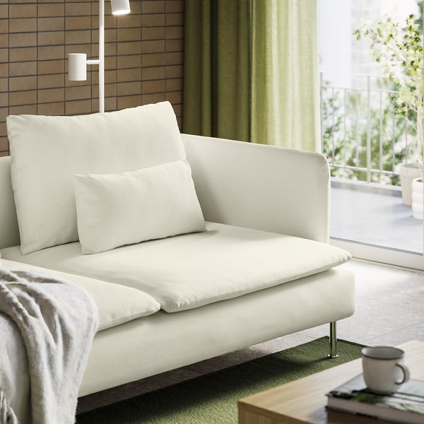 Modern white sofa with light green curtains, balcony view, coffee mug on table.