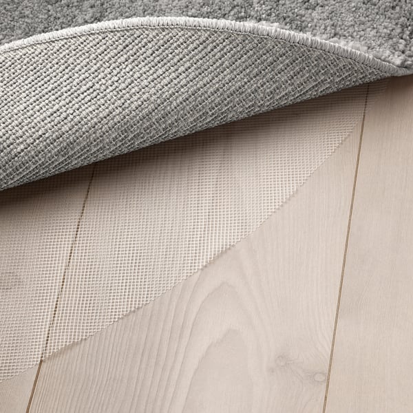 White area rug with a thick, soft pile, likely providing comfort and sound absorption, placed on a light wooden floor.