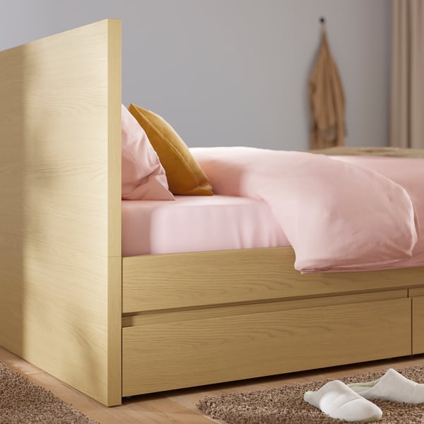 Bed frame with pink bedding and wooden drawers; sturdy and stylish with underbed storage.