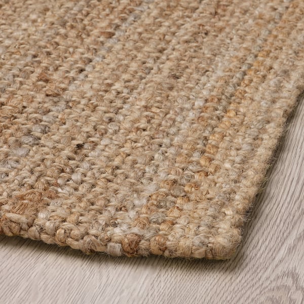 Natural jute rug close-up, shown on wooden flooring. Dense weaving, textured surface, robust yet stylish.