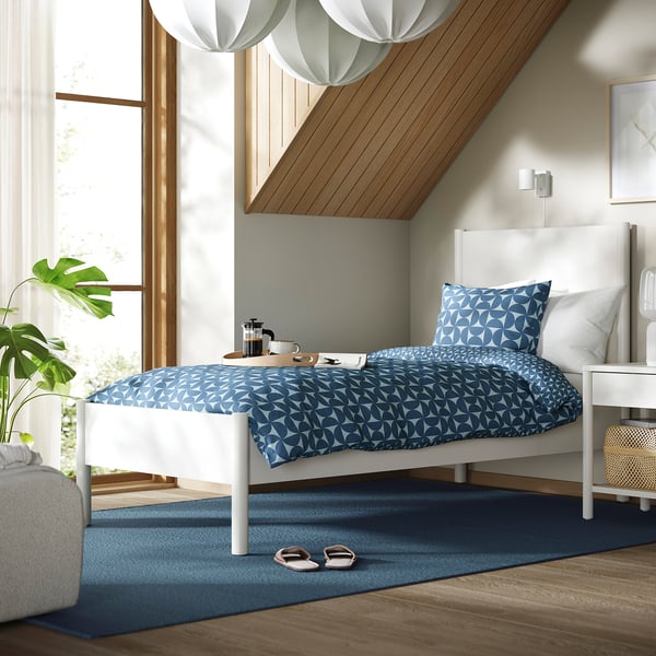 White bed with blue bedding, nightstands, coffee, plant, large window.