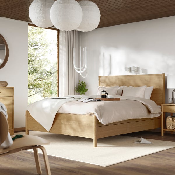 Minimalist bedroom with oak bed, soft-close drawers, three pendant lamps, rug, and large window.