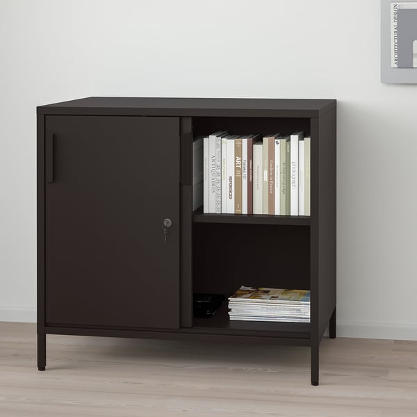 Black TROTTEN cabinet with sliding doors, open shelves, and adjustable feet in a room.