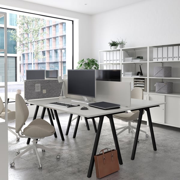 Modern office space with white TROTTEN desks, sleek computer monitors, ergonomic chairs, and organised shelves, featuring a city view.