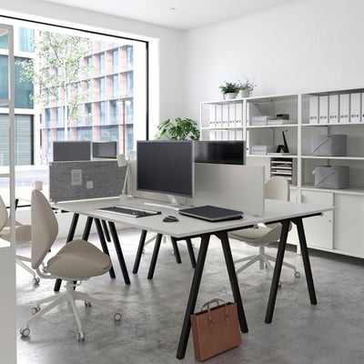 Modern office space with white TROTTEN desks, sleek computer monitors, ergonomic chairs, and organised shelves, featuring a city view.