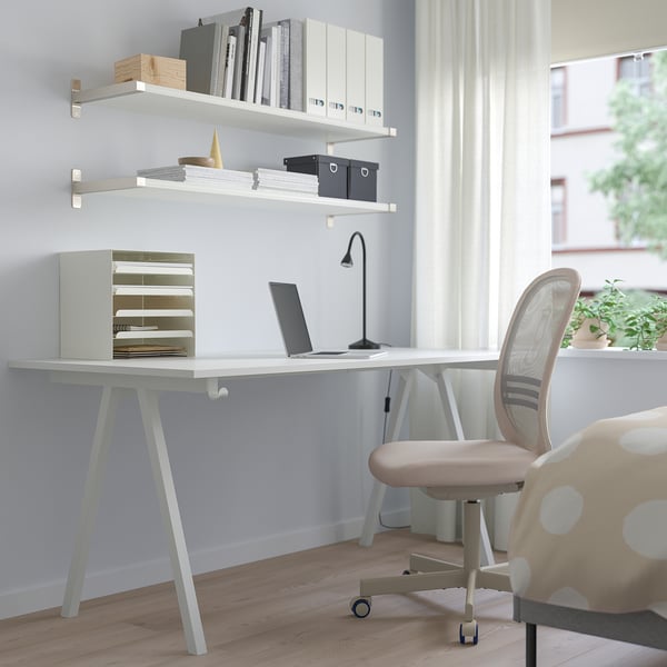 Modern troffen desk with a-legs, office chair, laptop, lamp, and books near window.