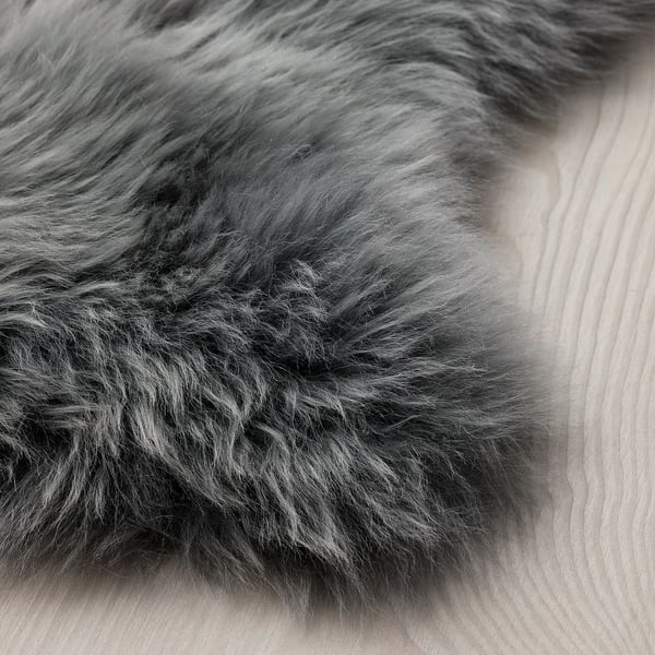 Fluffy, dark grey sheepskin rug on light wooden floor. Soft texture, inviting for touch.