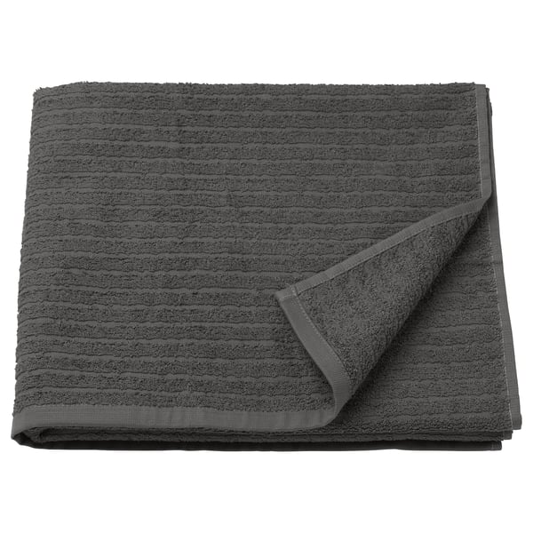 A dark grey VÅGSJÖN bath towel, rectangular with waffle texture and striped design, folded neatly. Made of 100% cotton.
