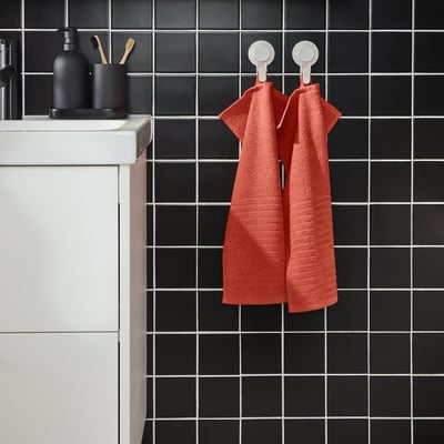 Red VÅGSJÖN towels hang on black-tiled wall, white sink left.
