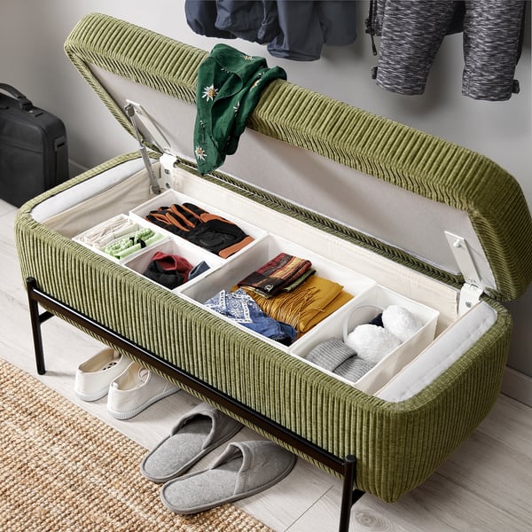 Green cushioned bench with metal legs, open lid revealing organised storage. Hinged lid supported by gas springs.