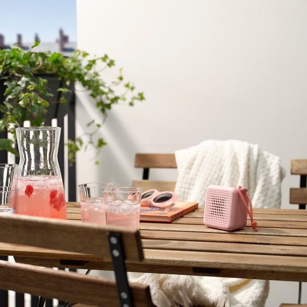 Pink portable speaker on table with drinks and plant