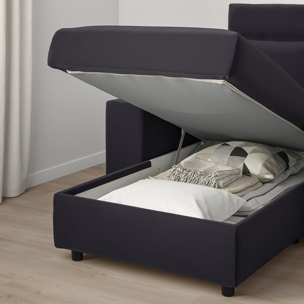 Dark grey sofa with lift-up seat revealing storage, showing cosy bedding inside.