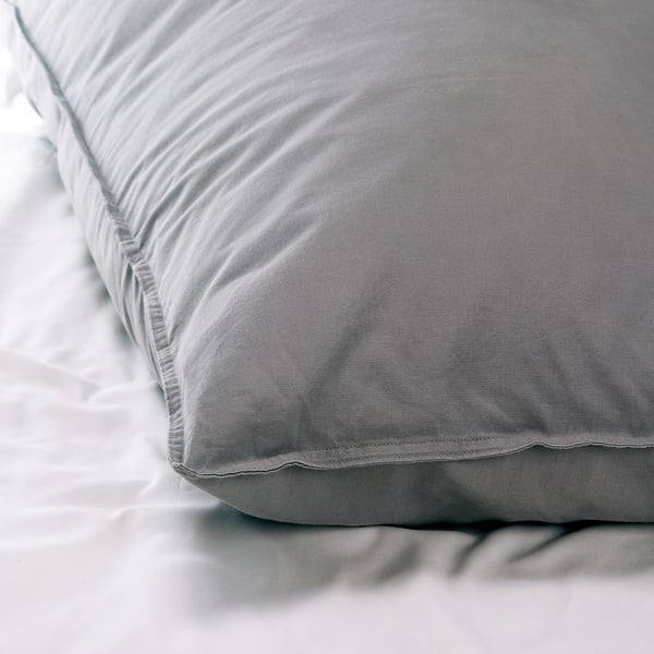 Soft, grey cotton bed sheet and pillowcase set on white bedding. High-quality, smooth fabric, inviting touch.