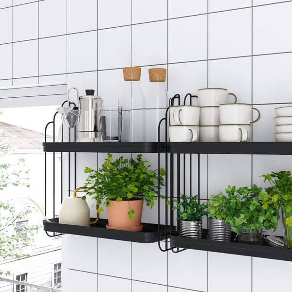 Modern black metal wall shelves hold white mugs, glass jars, and green plants in a white-tiled room, blending style with natural elements.