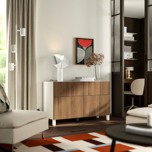 Modern minimalist room with BESTÅ sideboard, lamp, dried flowers, rug, armchair, window, and bookshelf.