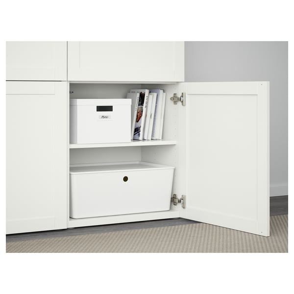 White BESTÅ cabinet with open door, showing adjustable shelves, a box, and magazines. Soft-closing hinges and push-opener function visible.