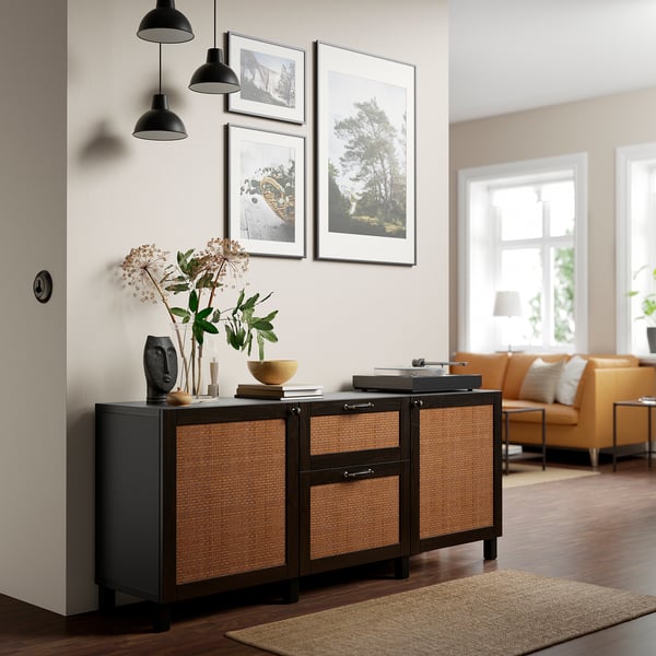 Wooden & rattan BESTÅ sideboard with lamps, flowers, & photos.