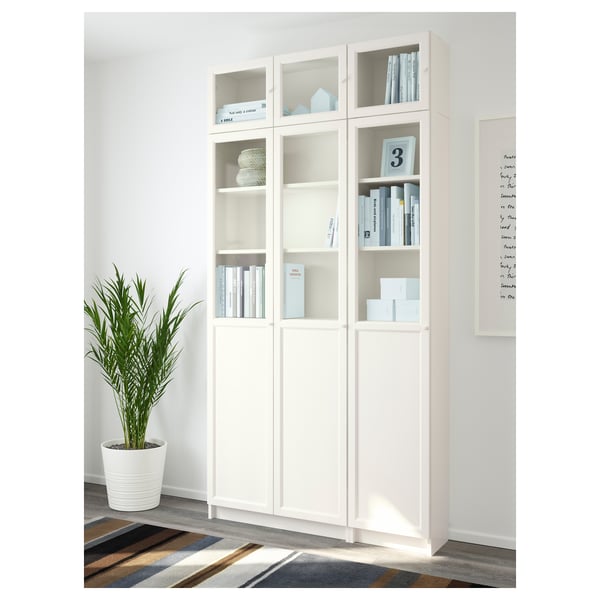 White BILLY bookcase with glass and panel doors. Displays books and hides clutter. Anchored to the wall for stability.