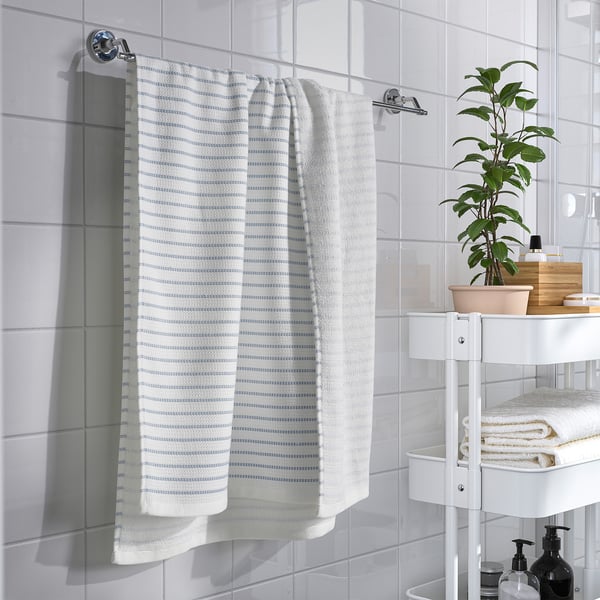 Modern bathroom with white tiles. BROKGINST towel, plants & toiletries. Natural light.