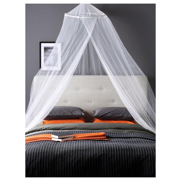 Bed with canopy, white netting, tufted headboard, colourful bedding, black wall with framed photo.