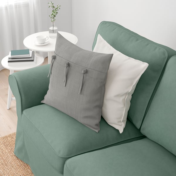 A cosy green sofa with soft cushions, a side table holding books and a teacup.