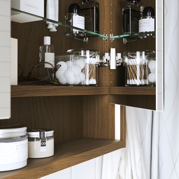 Wooden cabinet with mirror, built-in lighting around the edges, displaying bathroom essentials like cotton buds and bottles.