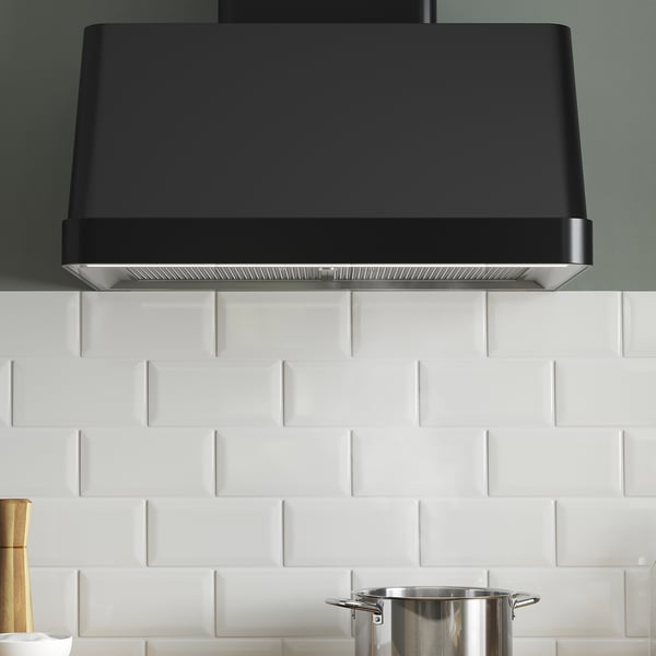 Modern black range hood with smooth curves, installed over white subway tiles, featuring built-in led lighting for cooking.
