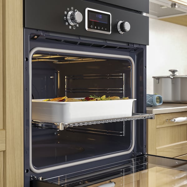 Black oven, baking dish with vegetables inside. Digital display, oven door open.
