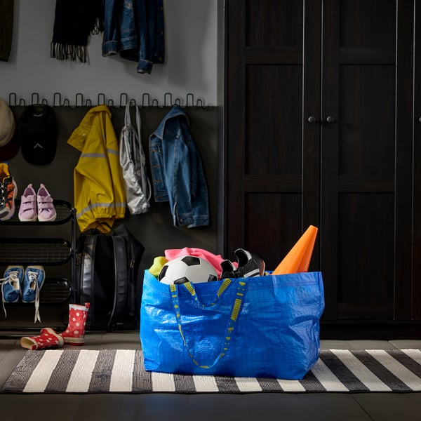 Blue reusable shopping bag filled with items, including a football ball, near a mudroom area with coat hooks, shoes, and jackets.
