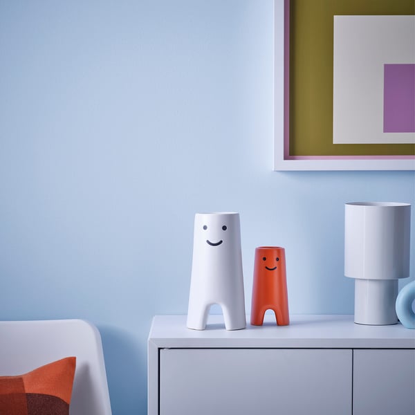 Two whimsical FRÖVÄXT vases, white with face design and orange, sit on a drawer in a modern setting.
