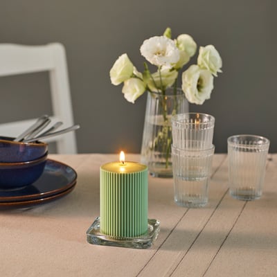 A table set with a lit candle, plates, glasses, and a vase of flowers. The candle provides atmospheric light.