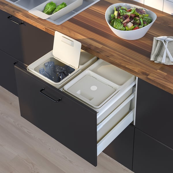 Modern kitchen cabinet with integrated recycling bins, wooden countertop, salad bowl, and grey tea towel.