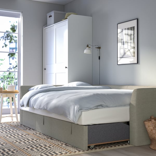 Bed by window, white linens, wall lamp, picture frame. Sofa transforms into bed, under-seat storage.
