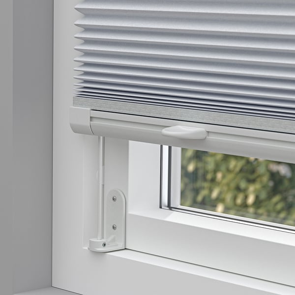 White pleated blind mounted on a window with light control, cordless handles for safety, versatile mounting options.