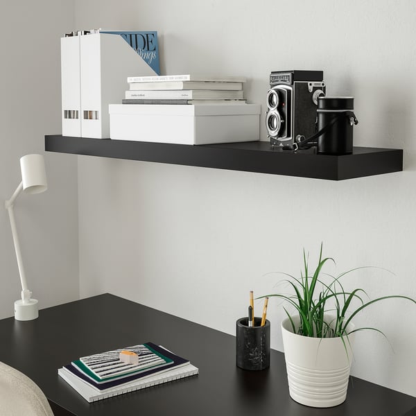 Find a sleek bLACK LACK wall shelf holding white books & vintage camera, paired with a bLACK desk featuring a stacked notebook & modern lamp.