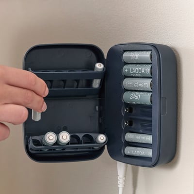 Person is placing a laada rechargeable battery into a grey charger box mounted on a wall.