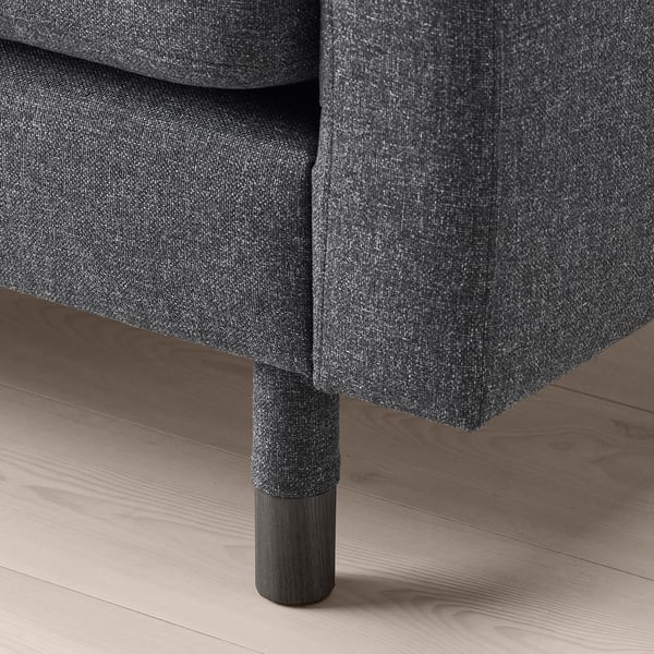 Dark grey upholstered sofa with wooden legs on hardwood floor.