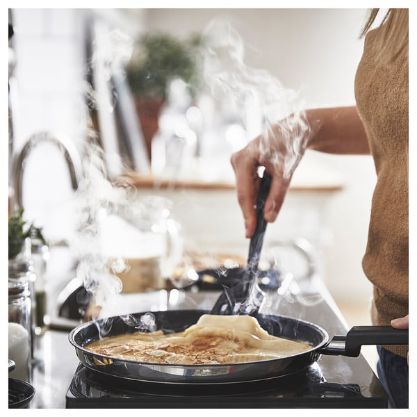 A person is cooking pancakes on a MIDDAGSMAT pan. Steam is rising. The pan is on a stove.
