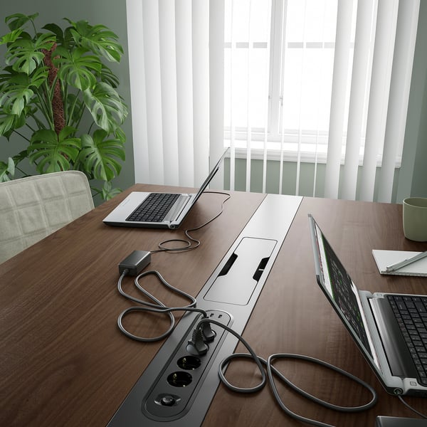 A modern conference table with integrated cable management, power sockets, and laptop connectors. Four hooks for bags or headphones are visible.